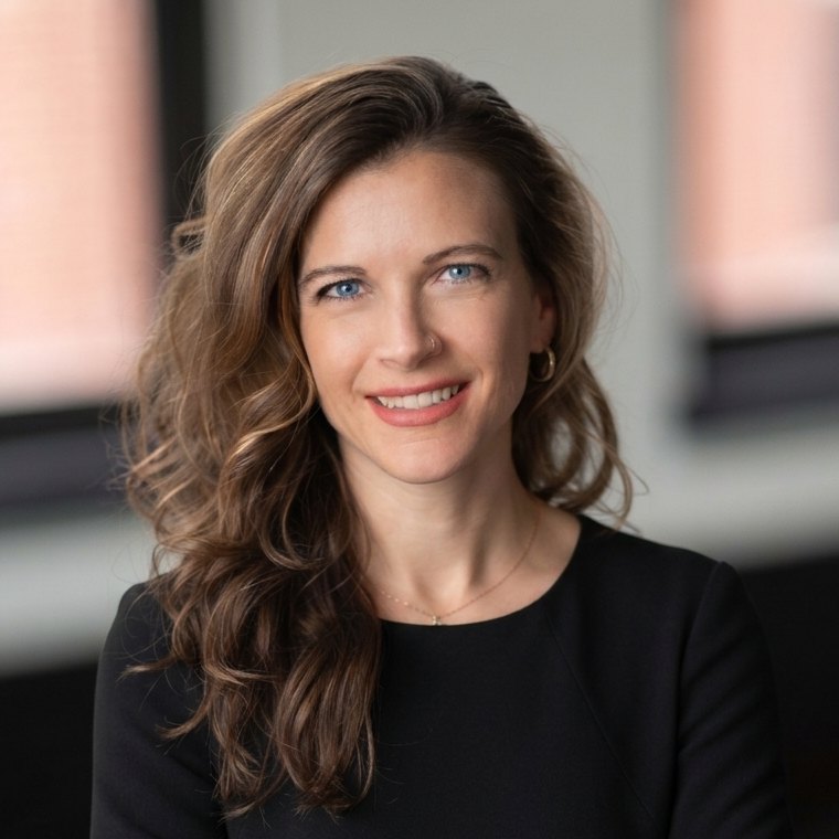 Amy Price, wearing a black top, smiling in an office with brick-framed windows