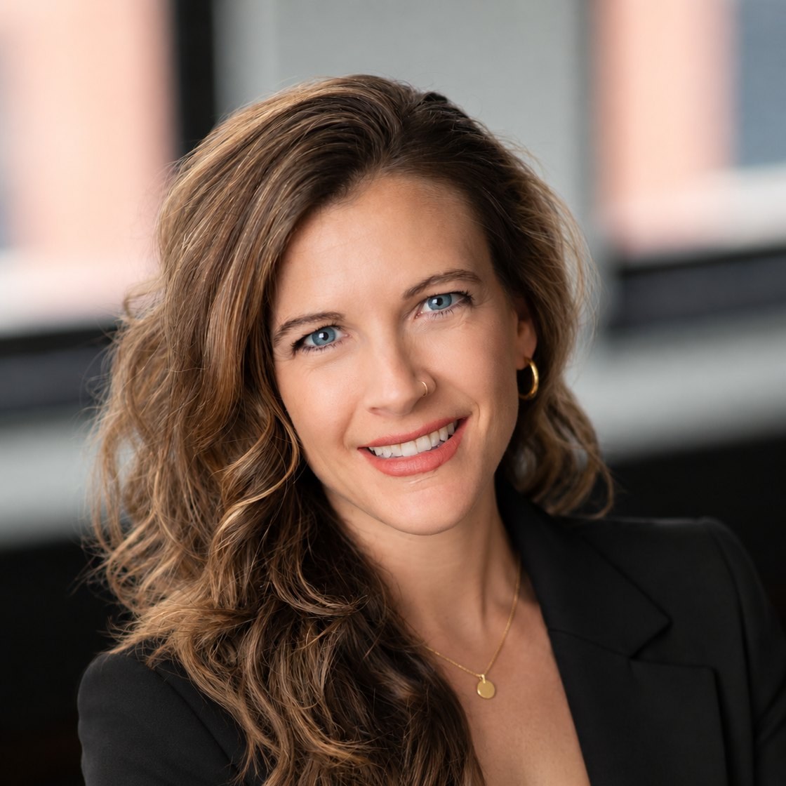 Amy Price, wearing a black blazer, smiling in an office with brick-framed windows