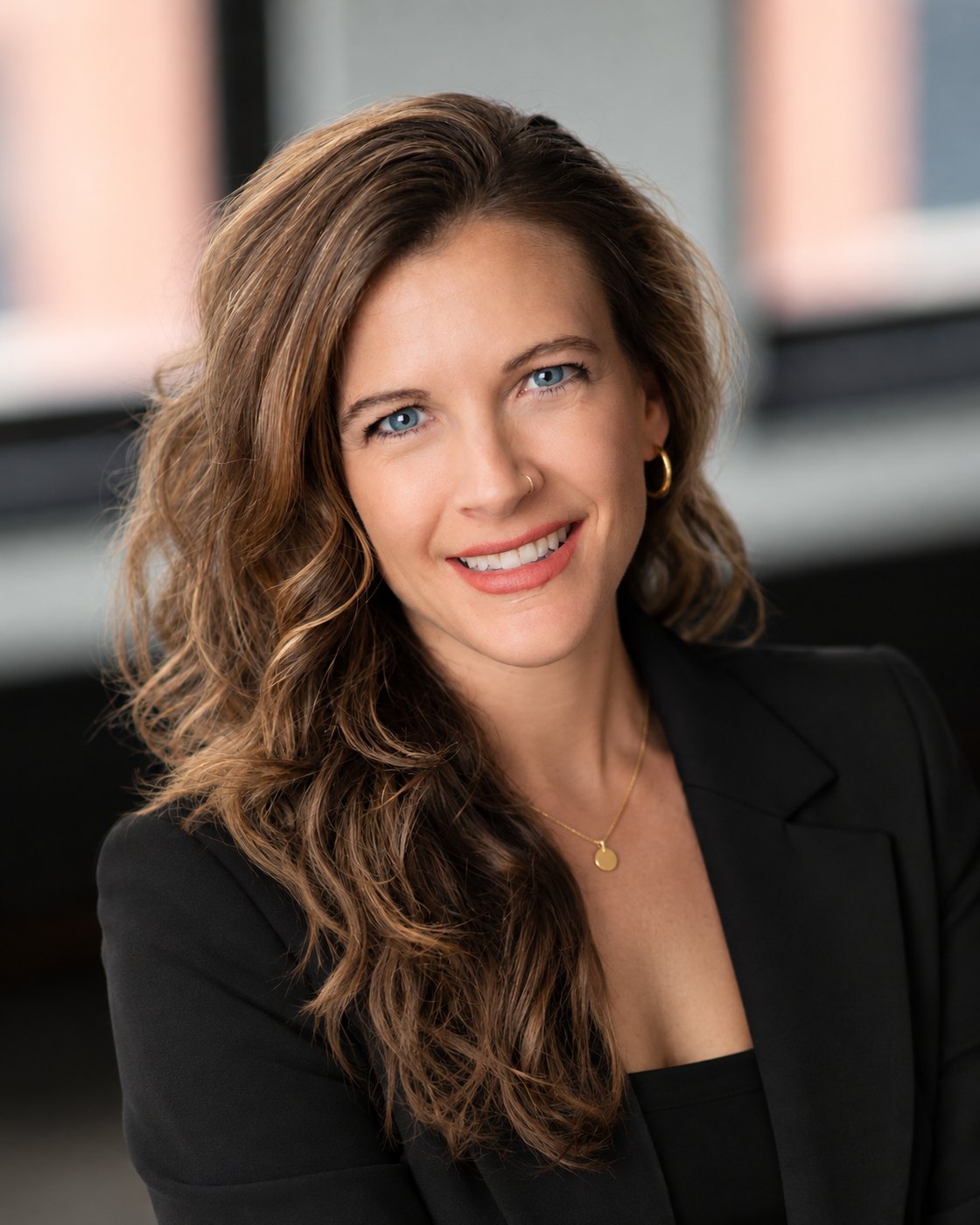 Amy Price, wearing a black blazer, smiling in an office with brick-framed windows